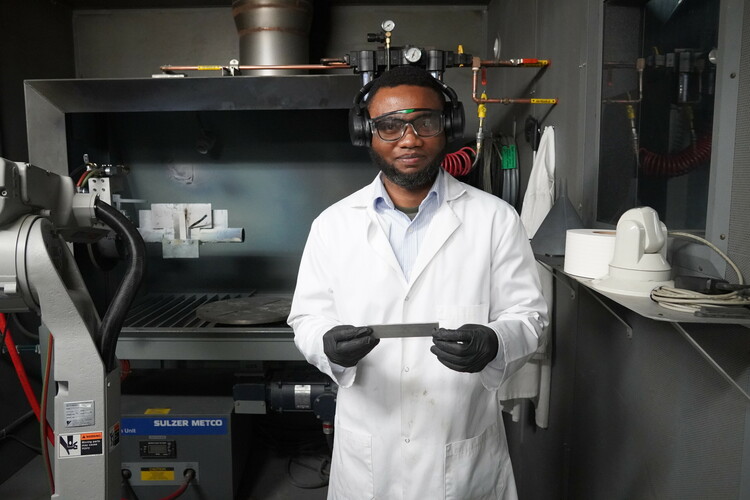 Research Assistant and PhD Candidate Adekunle Ogunbadejo presents a substrate sample in front of thermal spray equipment