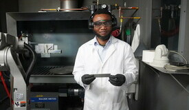 Research Assistant and PhD Candidate presents a substrate sample in front of thermal spray equipment