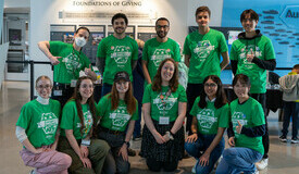 Eleven smiling people in green t-shirts form two lines for a group photo