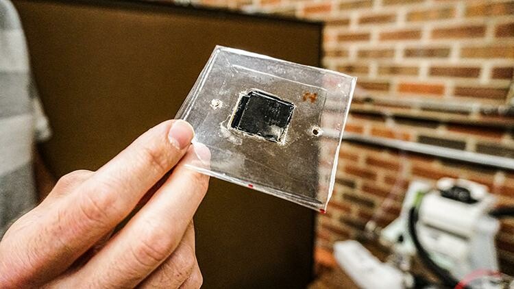 A man's hand holding a plastic square containing a smaller black square - the electrolyzer technology