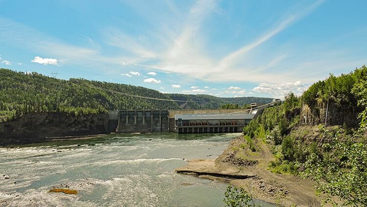 Looking up a river at a dam with trees and forest covering each river bank