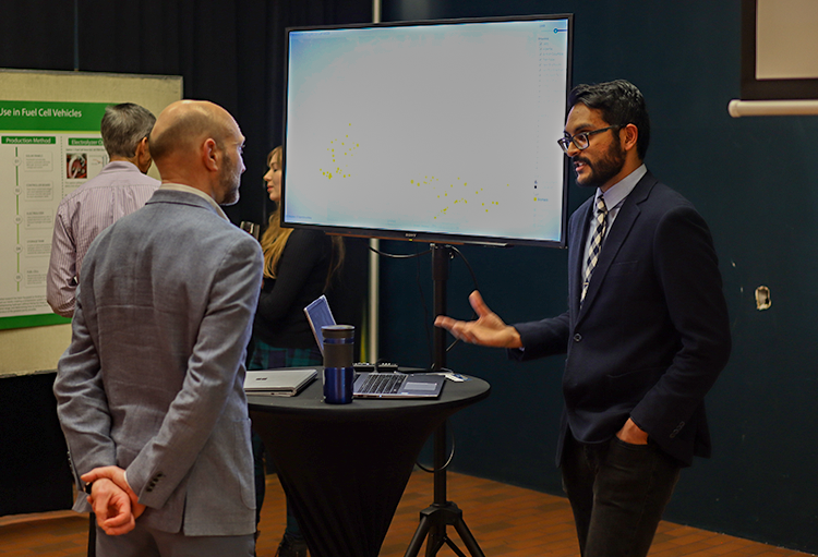 Sonak talks with a man in front of a screen displaying the Canadian Renewable Energy Project map.